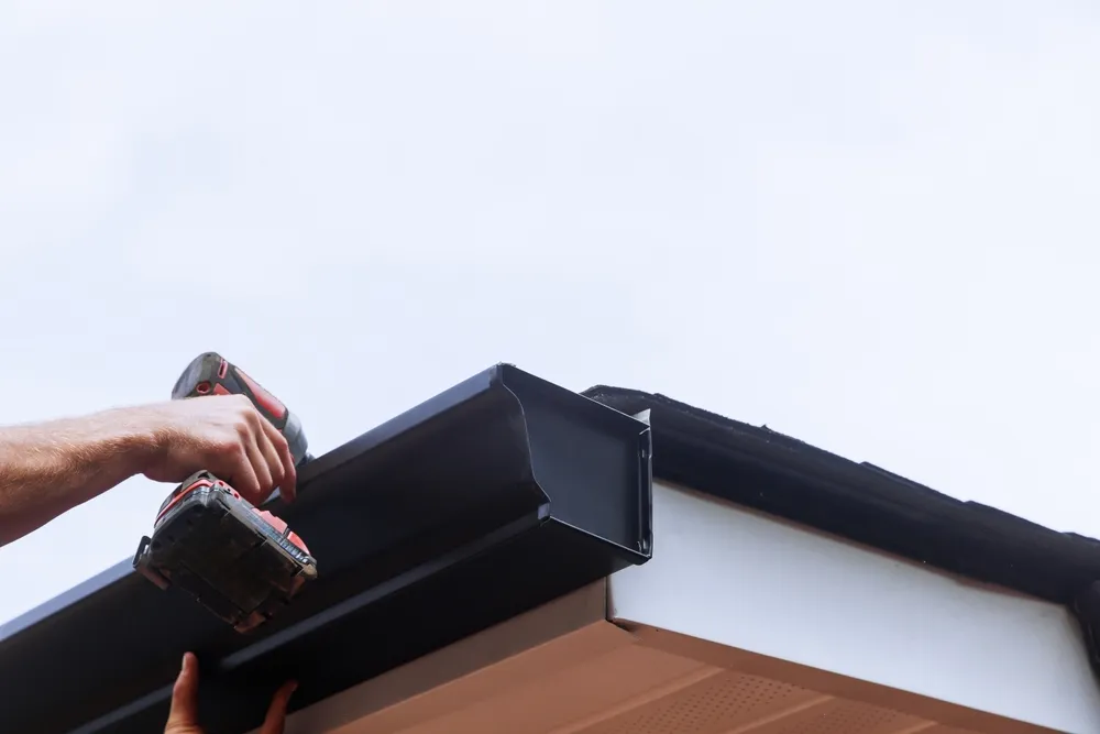 using drill to install black gutter on home
