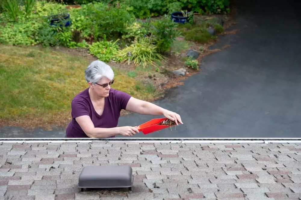woman cleaning out gutter with red gutter scoop