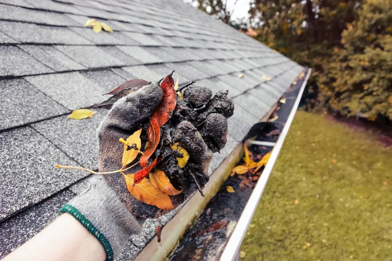 gloved hand clearing leaves and debris from gutter