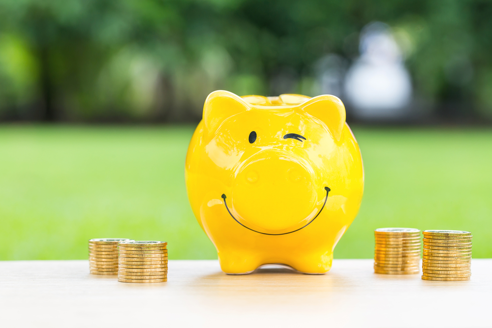 happy piggy bank next to stacks of coins